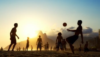 A Group Of People Playing Football On A Beach