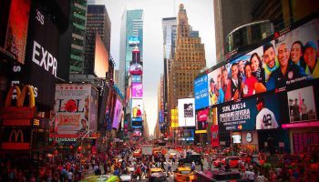 A Busy City Street With Many People And Billboards With Times Square In The Background
